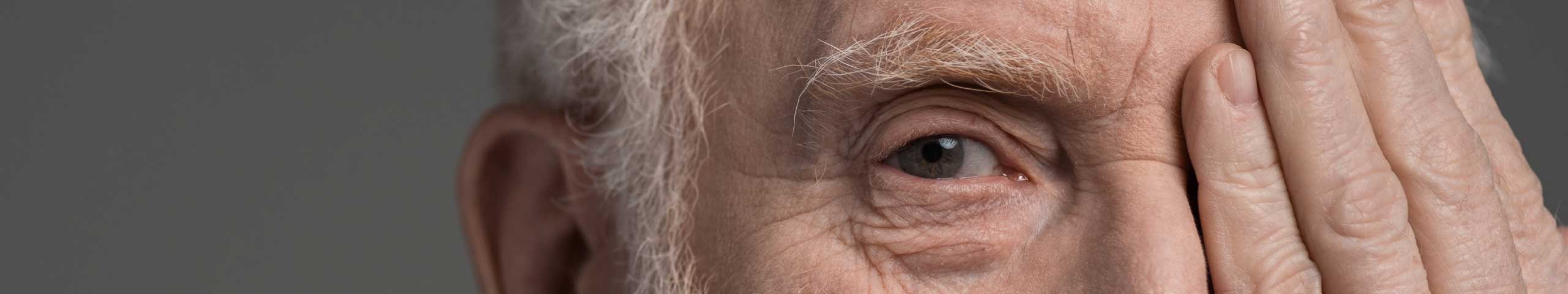 Older man with gray hair covering one eye with his hand